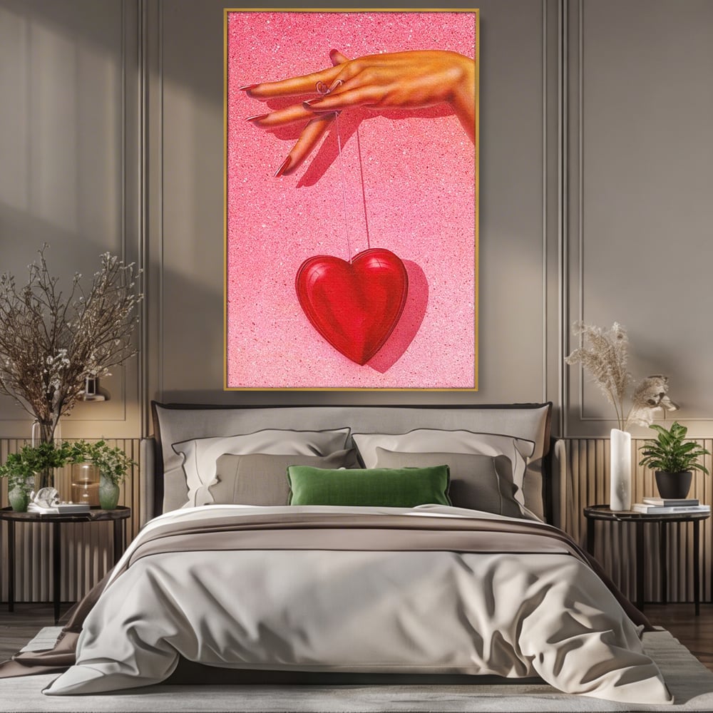 Tablou canvas cu ilustratie cu mana care tine o inima rosie, in rama de aluminiu auriu, pe perete intr-un dormitor