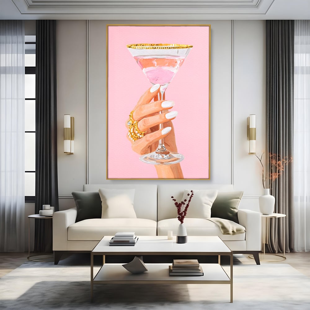 Tablou canvas cu ilustratie cu mana care tine pahar de cocktail, in rama de aluminiu auriu, pe perete intr-un living
