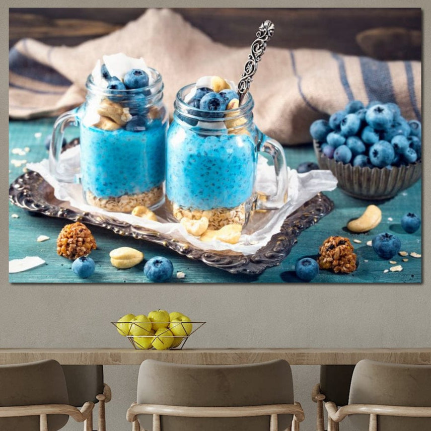 tablou canvas cu doua deserturi cu seminte de chia, afine si alune, pe o tava argintie, pe o masa albastru - turcoaz