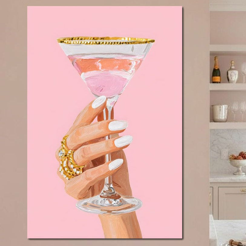 tablou canvas cu un pahar de cocktail, intr-o mana de femeie cu manichiura alba si bijuterii de aur, pe fundal roz pastelat