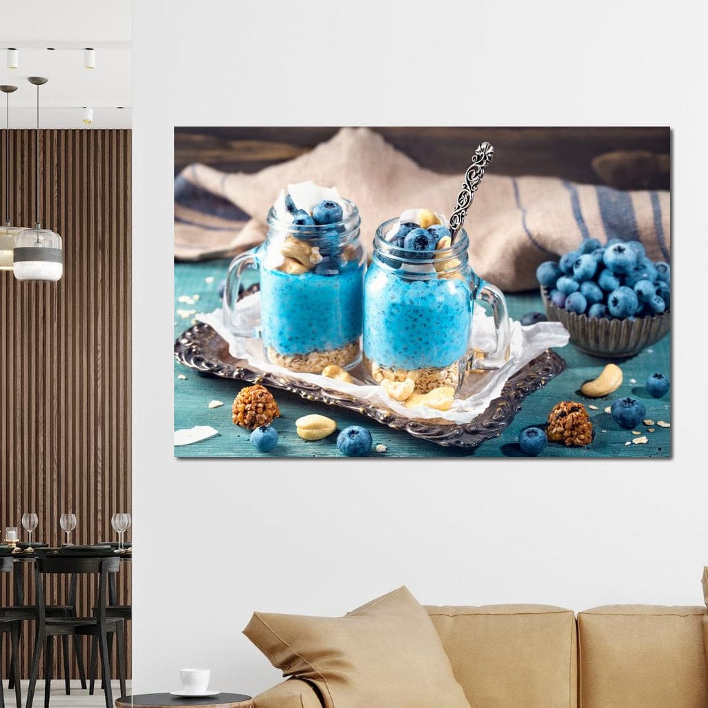 tablou canvas cu doua deserturi cu seminte de chia, afine si alune, pe o tava argintie, pe o masa albastru - turcoaz