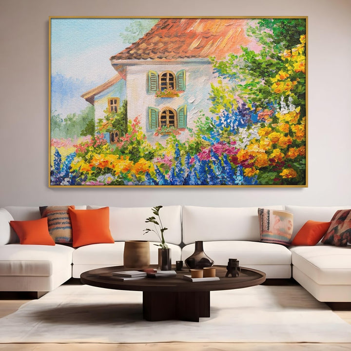 Tablou canvas cu pictura cu casa alba si flori, in rama de aluminiu auriu, pe perete intr-un living