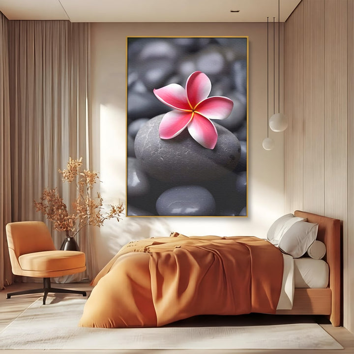 Tablou canvas cu floare roz pe pietre gri, in rama de aluminiu auriu, pe perete intr-un dormitor