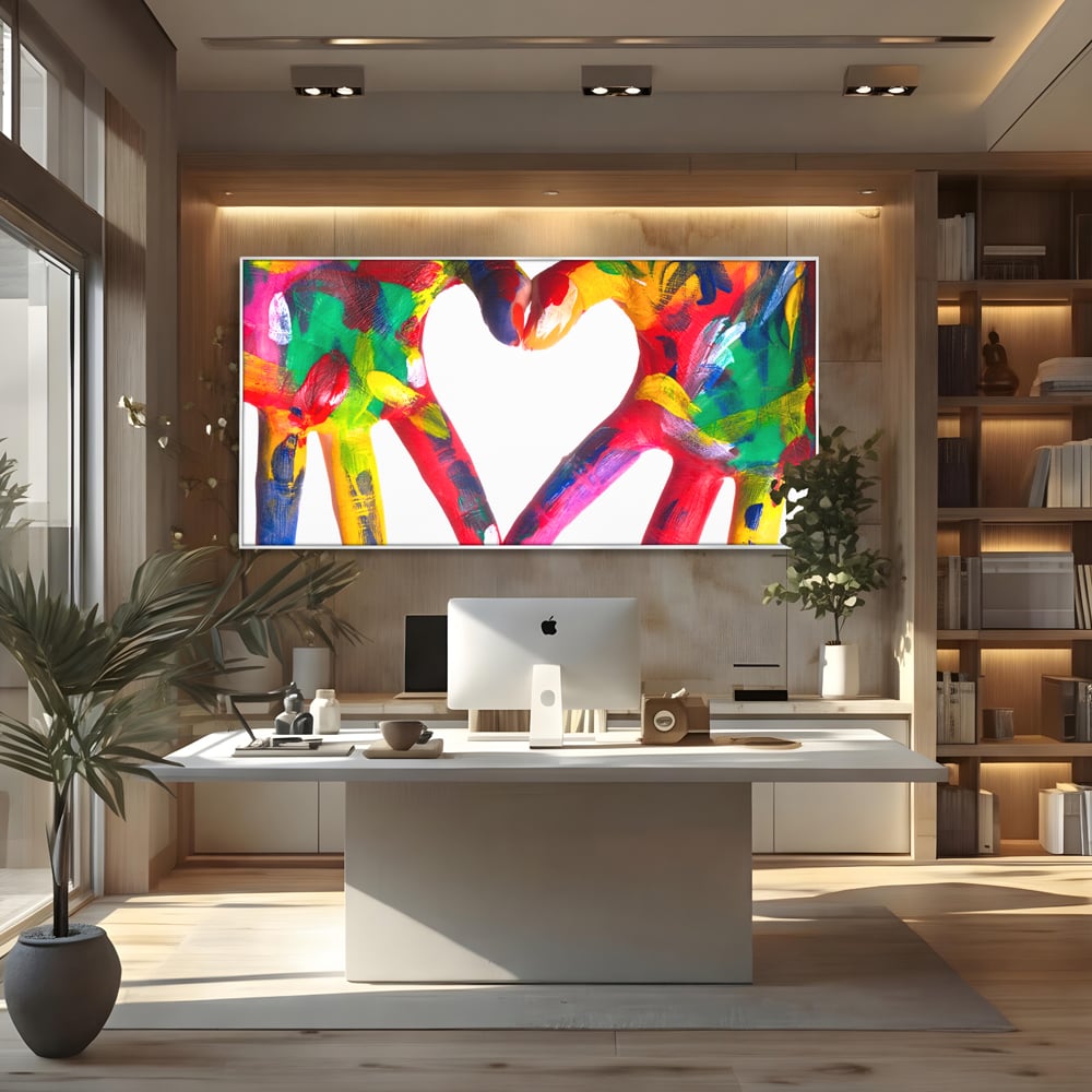 Tablou canvas cu pictura cu maini colorate formand o inima, in rama de aluminiu argintiu, pe perete intr-un birou