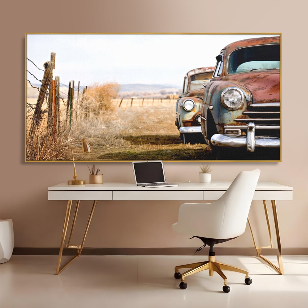 Tablou canvas cu doua masini ruginite pe un camp uscat, in rama de aluminiu auriu, pe perete intr-un birou