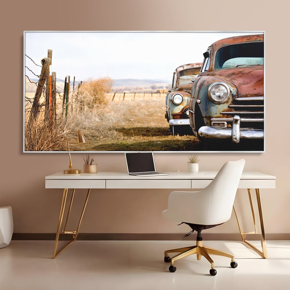 Tablou canvas cu doua masini ruginite pe un camp uscat, in rama de aluminiu argintiu, pe perete intr-un birou