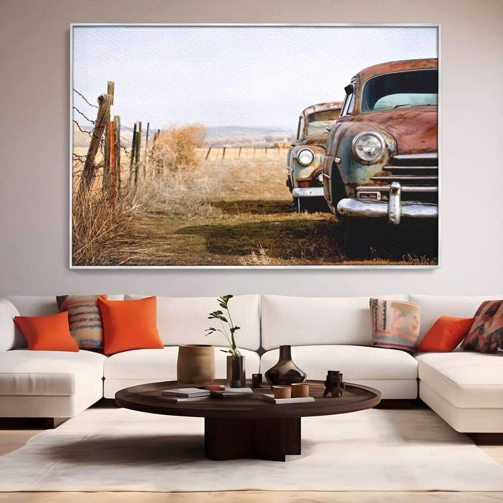 Tablou canvas cu doua masini ruginite pe un camp uscat, in rama de aluminiu argintiu, pe perete intr-un living