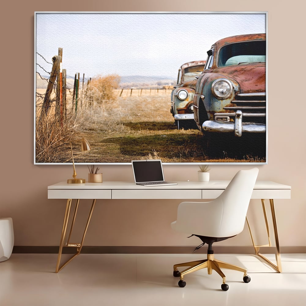 Tablou canvas cu doua masini ruginite pe un camp uscat, in rama de aluminiu argintiu, pe perete intr-un birou