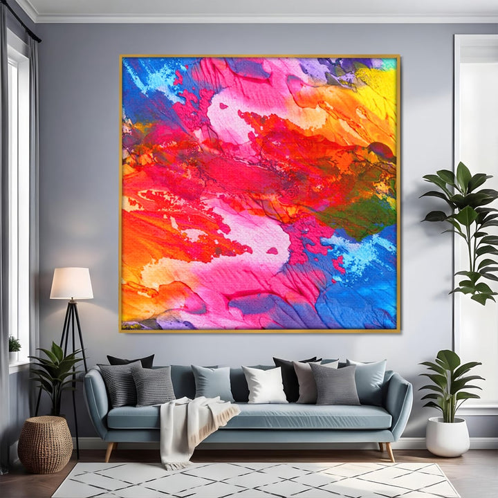 Tablou canvas cu pictura abstracta cu pete de culoare, in rama de aluminiu auriu, pe perete intr-un living