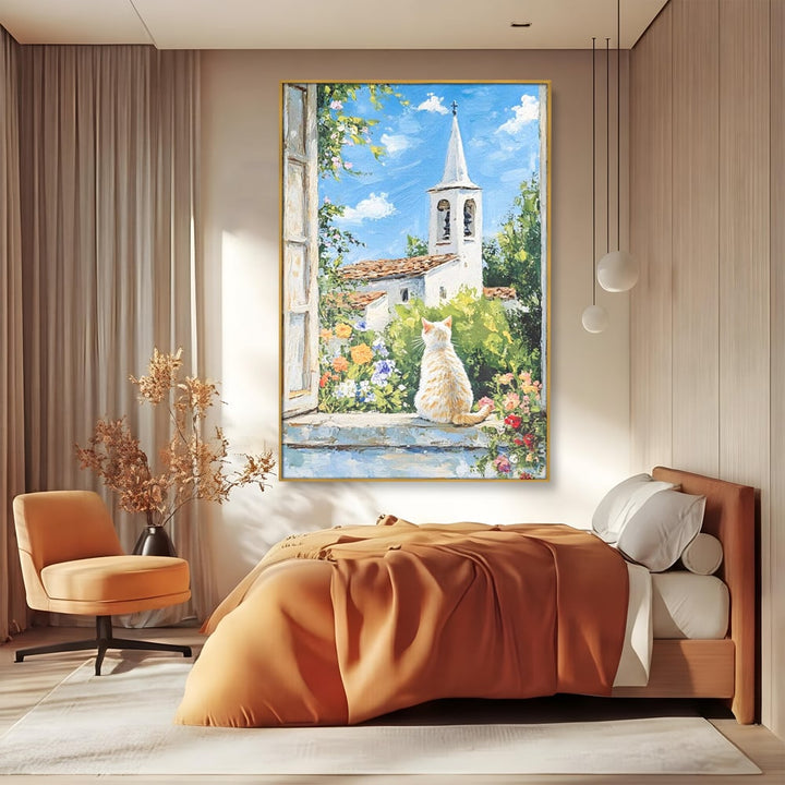 Tablou canvas cu tablou pictura cu pisica alba si biserica, in rama de aluminiu auriu, pe perete intr-un dormitor
