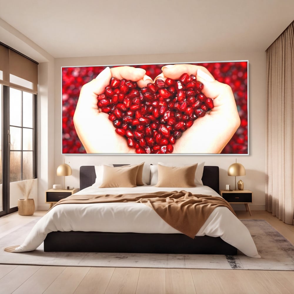 Tablou canvas cu maini care tin seminte de rodie in forma de inima, in rama de aluminiu argintiu, pe perete intr-un dormitor