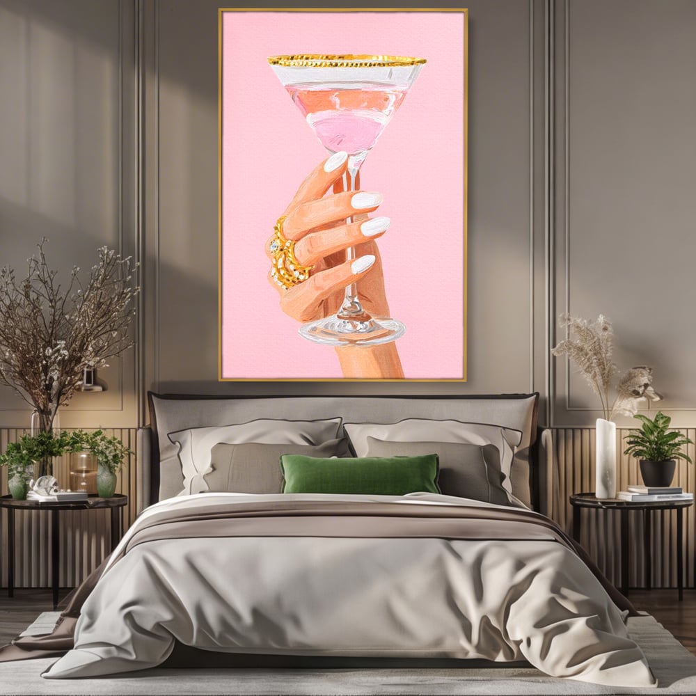Tablou canvas cu ilustratie cu mana care tine pahar de cocktail, in rama de aluminiu auriu, pe perete intr-un dormitor