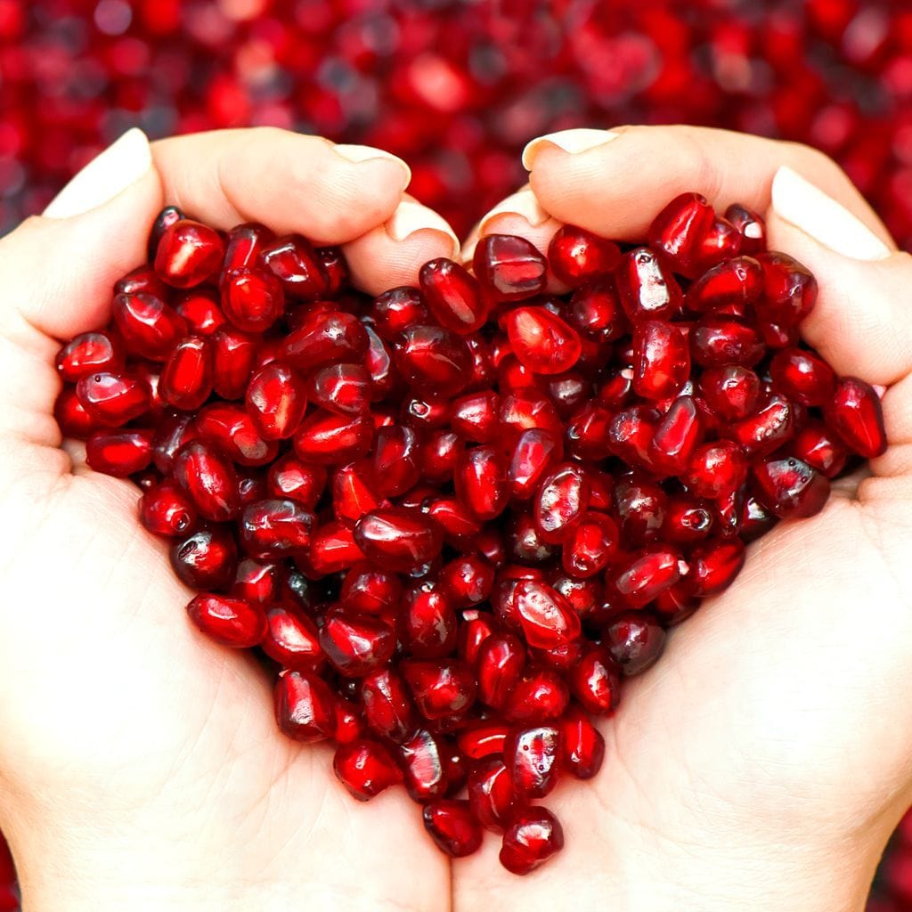 tablou canvas cu seminte de rodie, cuprinse intre doua maini, pe fundal rosu