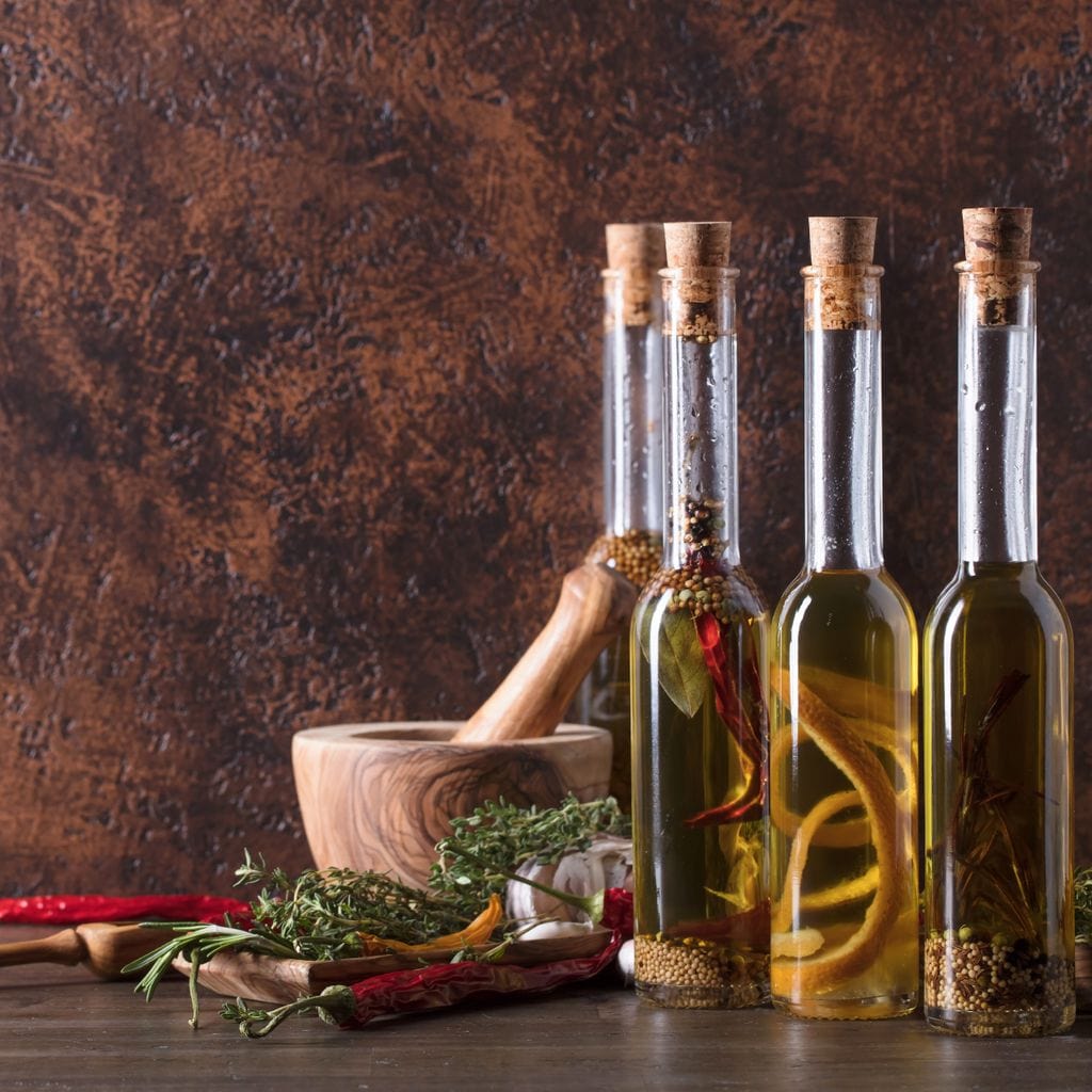 tablou canvas cu sticle de ulei pe o masa cu diverse mirodenii si verdeturi, intr-un cadru rustic de bucatarie