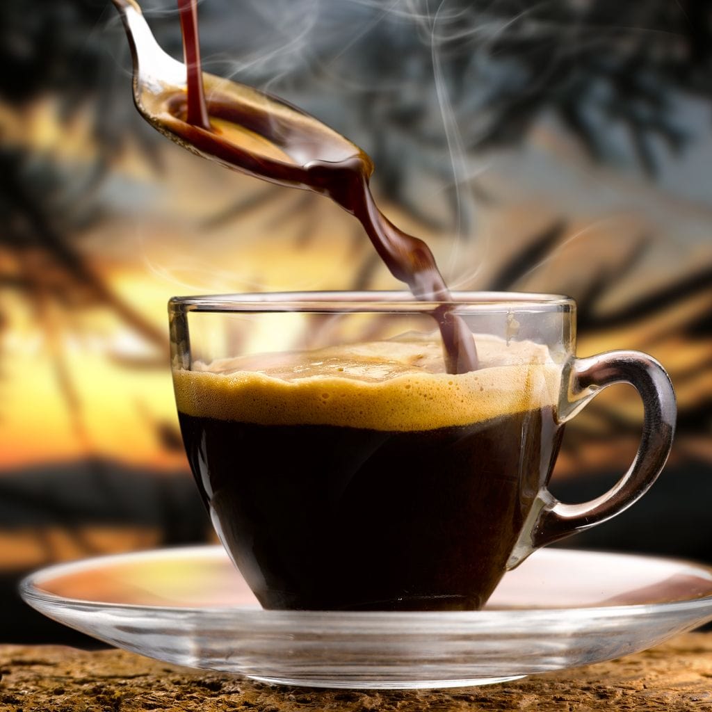 tablou canvas cu un espresso fierbinte, turnat intr-o ceasca transparenta, pe fundal tropical la rasarit