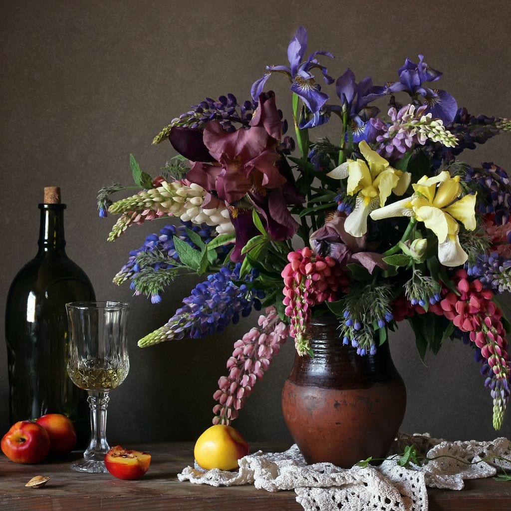 tablou canvas cu o vaza cu flori colorate, pe o masa cu o sticla de vin, un pahar si fructe, intr-un cadru rustic