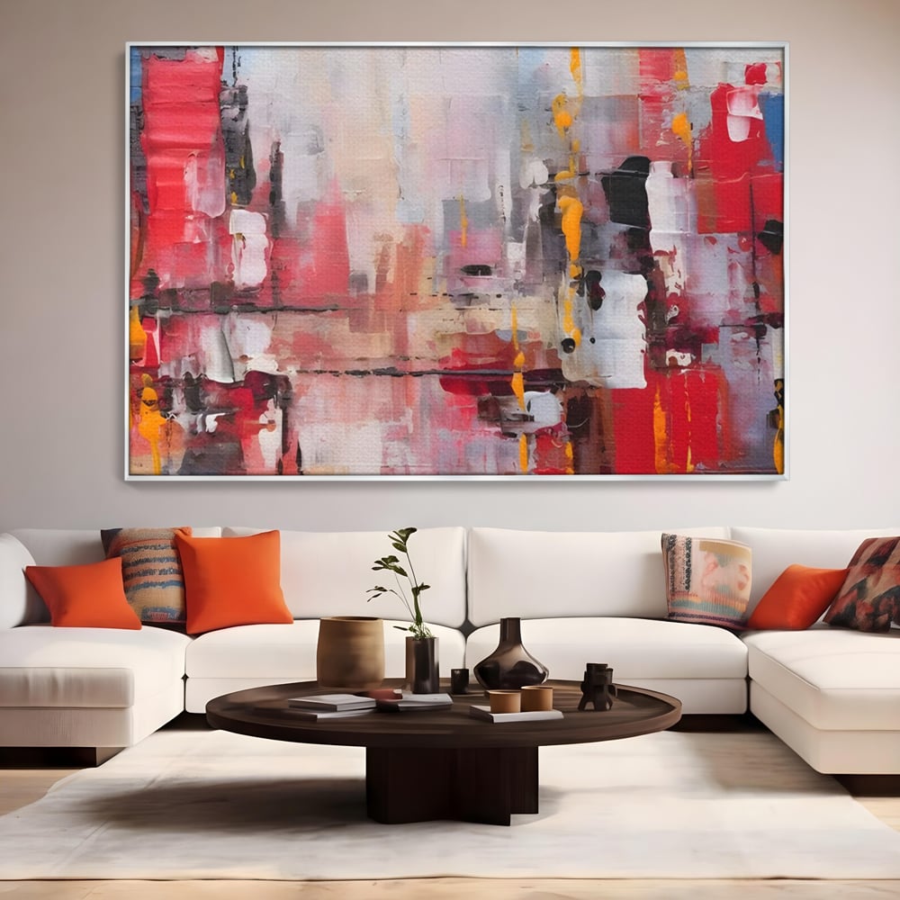 Tablou canvas cu pictura abstracta cu pete de rosu si galben, in rama de aluminiu argintiu, pe perete intr-un living